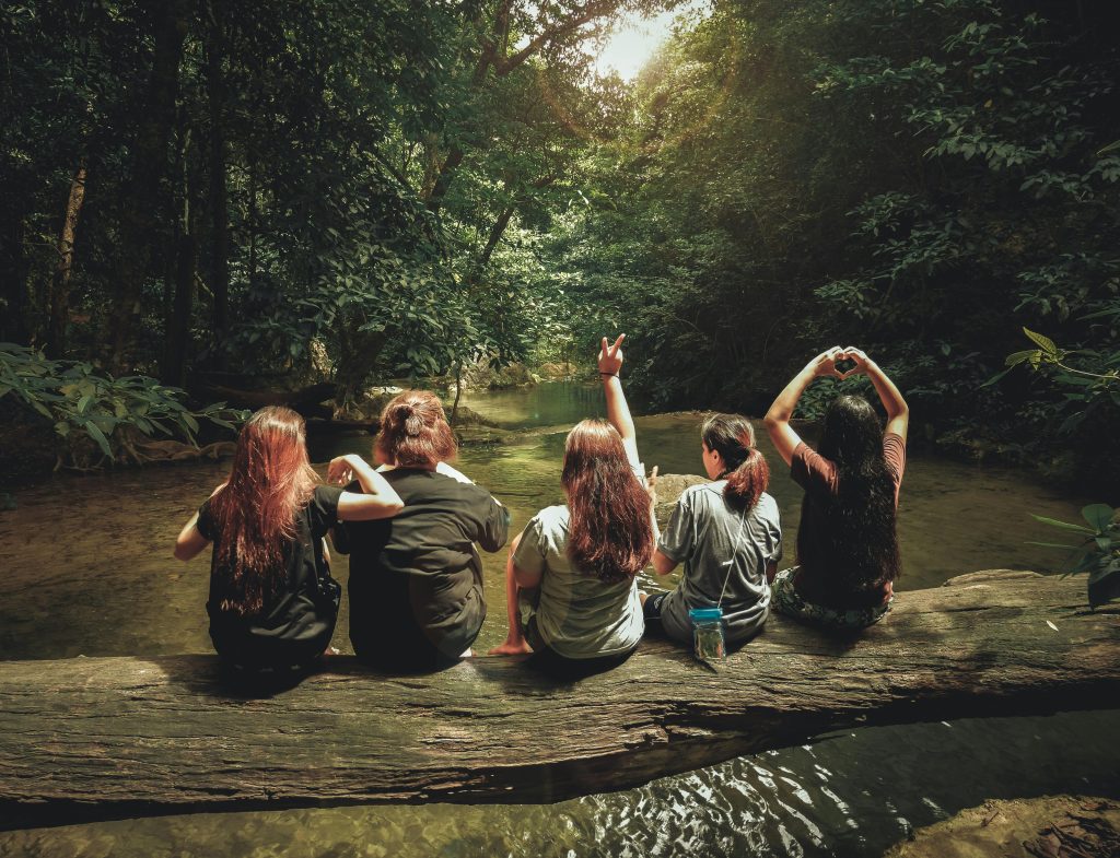 group of people sitting on a tree trunk over a river